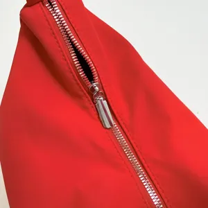 Close-up detail of red fabric crossbody bag with smooth silver zipper and durable stitching.