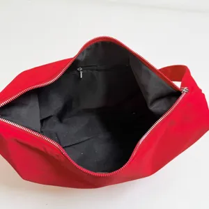 Red nylon crescent shoulder bag interior detail showing black fabric lining and zip pocket.
