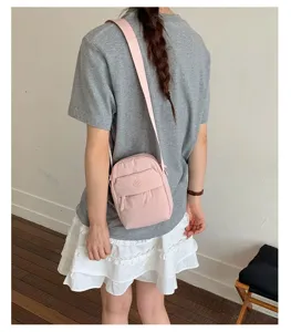 Close-up view of a pink casual crossbody bag worn by a model in a clean indoor daily scene.