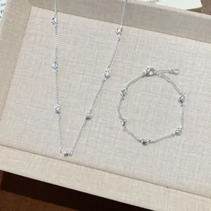 Delicate silver heart charm necklace and bracelet set, elegant minimalist jewelry detail.