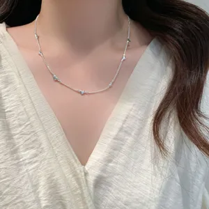 Close-up detail of a delicate silver chain necklace with multiple small heart charms worn on neck.