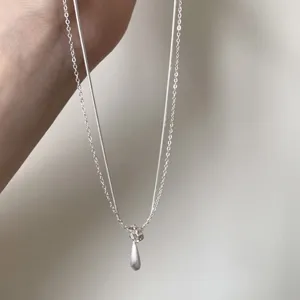 Close-up detail of a minimalist double-layered silver necklace with a delicate teardrop pendant.
