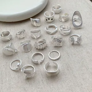 Primer plano detallado de anillos geométricos irregulares de plata mate sobre tela.
