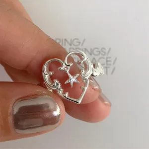 Detaillierte Nahaufnahme des silbernen hohlen Herzrings mit hängendem Stern-Anhänger.