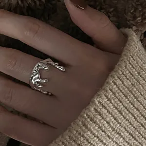 Nahaufnahme eines unregelmässigen silbernen Tropfenrings am Finger, stylisches minimalistisches Detail.