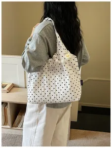 Close-up detail of white canvas shoulder bag featuring black polka dots and pearl strap.