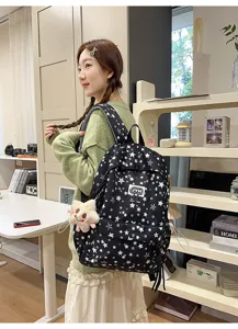 Detailed view of a black multi-compartment backpack with white star patterns, worn by a model.