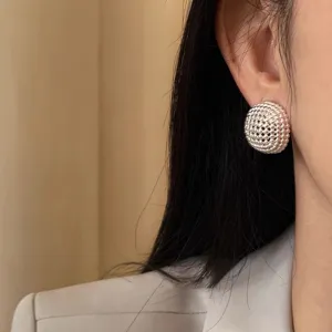 Close-up detail of silver woven domed button stud earrings, elegant retro texture design.