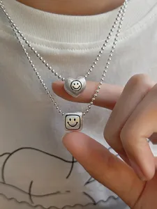Detail shot of double layer silver bead chains with matte heart and cube smiley pendants.