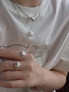 Close-up detail of brushed silver geometric smile heart and cube necklace and ring set.