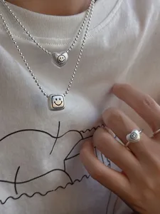 Close-up detail shot of brushed matte geometric smiley face heart necklace and ring set.