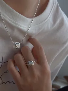 Detail shot of matte silver smiley face square pendant necklace and matching ring set.