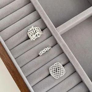 Detailed view of silver geometric hollow lattice and braided rings placed inside velvet box.