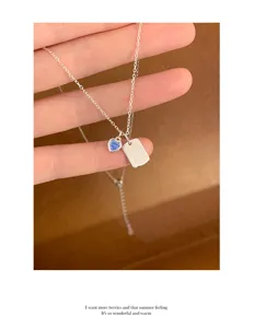 Detailed view of silver clavicle chain featuring a blue heart pendant and engraved square tag.