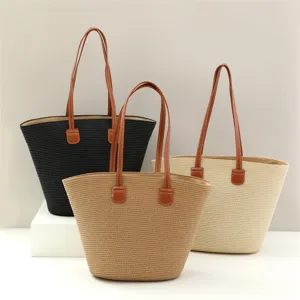 Detalle de bolso tote de paja tejida con textura y asas de cuero marrón para verano.