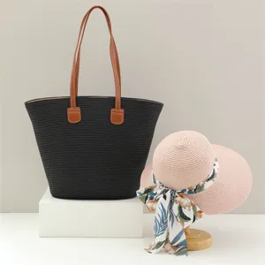 Bolso tote de paja negra y sombrero de sol rosa para vacaciones playa verano chic.