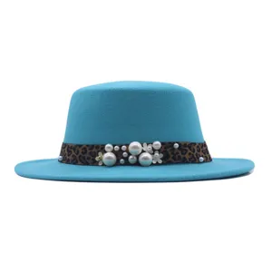 Detalle de sombrero fedora plano turquesa con banda de leopardo, perlas falsas y flores blancas