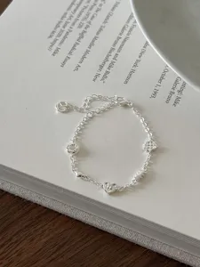 Detailed view of dainty silver bracelet with croissant and heart charms on a book.