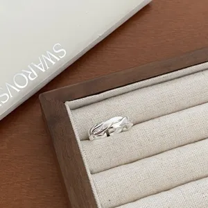 Close-up detail of silver geometric open ring displayed in a beige linen jewelry tray.
