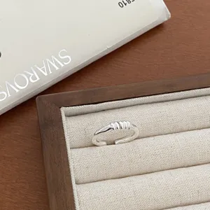 Close-up detail shot of a silver open geometric ring with textured ribbed center on tray
