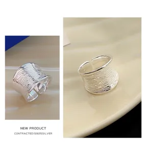Close-up detail of wide silver ring, geometric wavy texture, adjustable open design.
