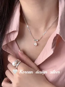 Gros plan détail du collier argenté à plusieurs brins de perles et de sa bague assortie.