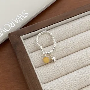 Detailed closeup shot of silver bead ring featuring a yellow ball and small bell pendant.