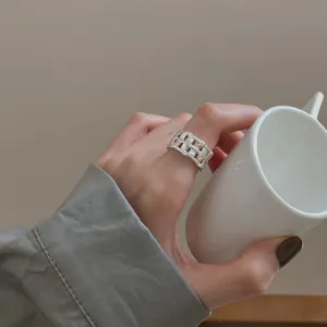 Close-up detail of a wide woven geometric silver ring worn on a hand holding a ceramic cup.
