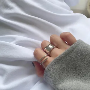 Close-up detail shot of geometric silver open rings worn on finger, minimalist street style.