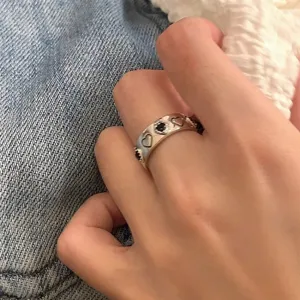 Close-up detail of silver metal heart ring, featuring engraved and black stone heart motifs.