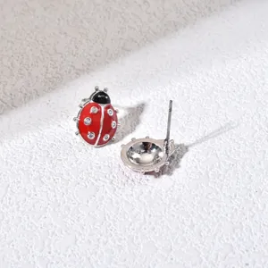Close-up detail of cute ladybug stud earrings featuring red enamel and sparkling rhinestones.