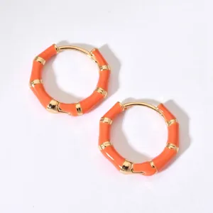 Nahaufnahme im feinen Detail von leuchtend orangen Bambus-Creolen mit goldenen Akzenten.