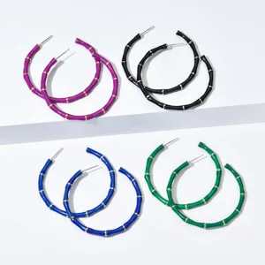 Gros plan de boucles d'oreilles créoles colorées en forme de bambou, violet, noir, bleu et vert.