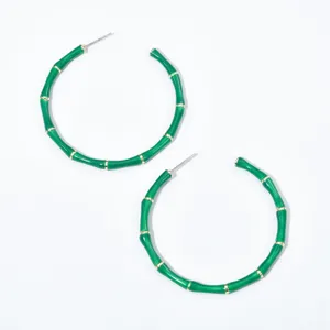 Gros plan détaillé de boucles d'oreilles créoles en bambou vert avec des accents dorés.