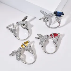 Nahaufnahme eleganter silberner Kolibri-Ringe mit funkelnden Kristallen und bunten Edelsteinen.