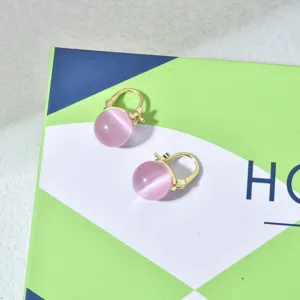 Nahaufnahme von rosa Katzenauge Ohrringen mit goldener Fassung auf geometrischer Schachtel.