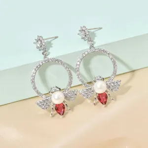 Close up of exquisite bee drop earrings with shiny zircon, pearl and red stone details.
