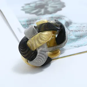 Detailed close-up of a chunky woven multi-metal wire bracelet featuring gold, silver, and black tones.