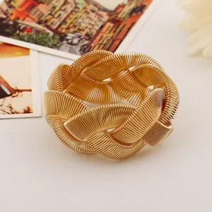 Close-up of a chunky gold metal woven bracelet, featuring a heavy metal spring design for bold fashion.
