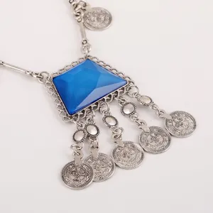 Dettaglio in primo piano della collana con monete vintage, gemma blu e nappe pendenti.