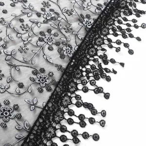 Gros plan sur un tissu en dentelle noire brodée de fleurs, sequins brillants et bordure de franges.
