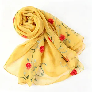 Close-up detail of a yellow chiffon scarf with delicate red rose embroidery and green stems.