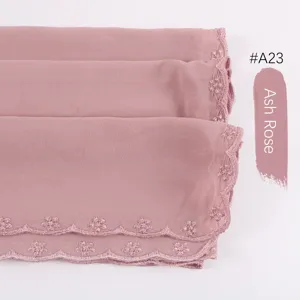Detalle del hiyab de gasa rosa ceniza con delicados bordes de encaje bordados y ondas.