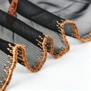 Close up of exquisite black mesh fabric featuring metallic gold embroidered wavy lace edge trim.