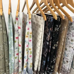 Detail view of various floral and geometric print voile headscarves hanging on wooden racks.
