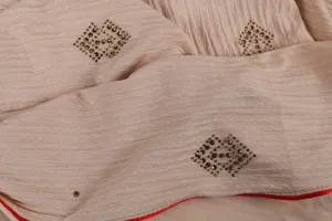 Detailed close-up of breathable pleated beige hijab scarf with sparkly rhinestones and red trim.