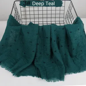 Detail view of the crinkled cotton linen scarf with pom pom and frayed edge in deep teal color.
