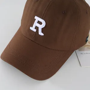 Dettaglio cappellino da baseball marrone con ricamo lettera R bianca e visiera curva.