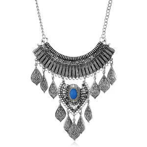 Close-up of vintage metal bib statement necklace with leaf engravings, blue stone and fringe.
