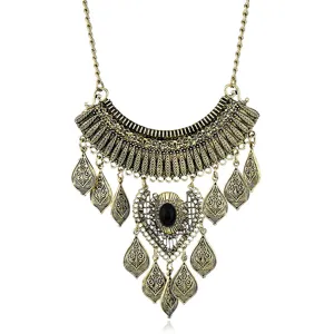 Close-up of vintage gold metal statement necklace featuring carved leaf tassels and black stone.